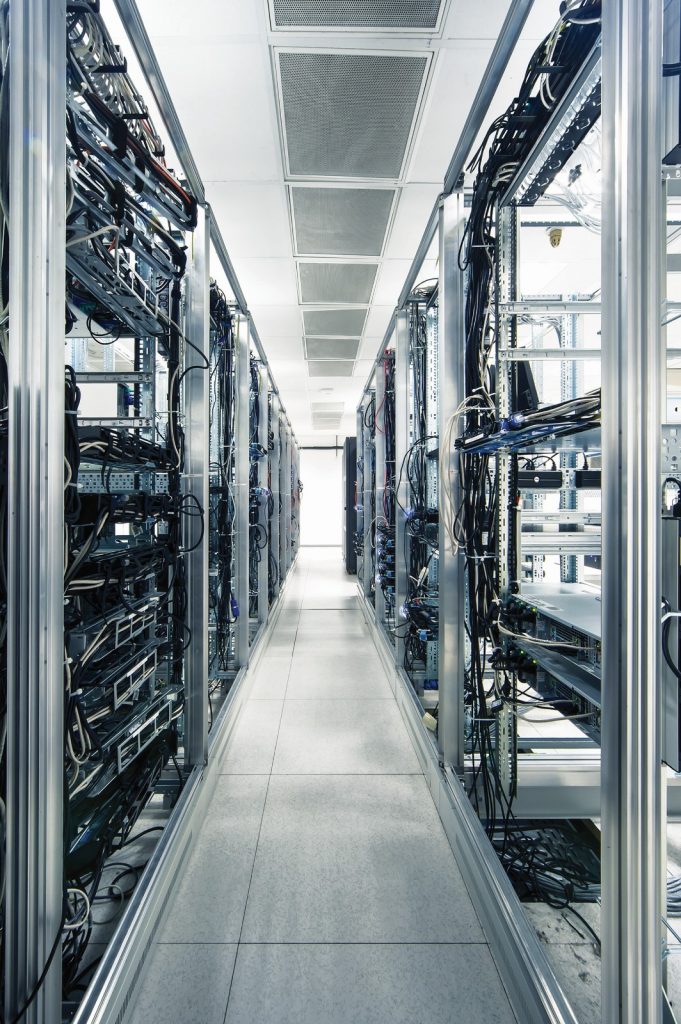 Ein Innenansicht eines Serverraums mit Reihen von Servern und Kabeln, die entlang der Seitenwände verlaufen.